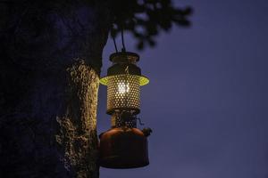 lampe à huile vintage accrochée à un arbre dans la forêt dans l'atmosphère de camping du soir, concept de plein air de voyage photo