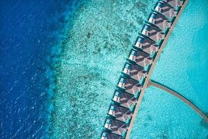 vue aérienne de dessus des villas avec piscine, bungalows sur la plage tropicale paradisiaque des maldives. incroyable lagon bleu turquoise de la mer, eau de la baie de l'océan. destination de vacances de voyage de luxe. beau paysage aérien ensoleillé photo