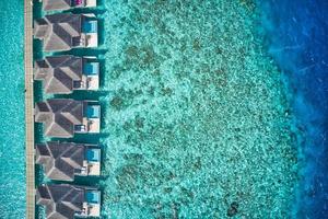 vue aérienne de dessus des villas avec piscine, bungalows sur la plage tropicale paradisiaque des maldives. incroyable lagon bleu turquoise de la mer, eau de la baie de l'océan. destination de vacances de voyage de luxe. beau paysage aérien ensoleillé photo