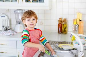 Funny kid boy aidant et laver la vaisselle à la maison