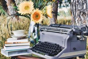 machine à écrire grise vintage, un vase de tournesols, une pile de livres et une tasse de thé sur une table photo