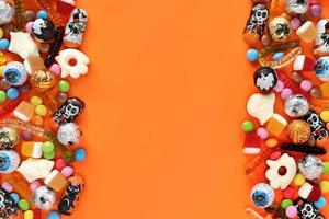 fond orange halloweem avec espace de copie au milieu, bonbons assortis des deux côtés - chocolats traditionnels aux globes oculaires, vers de gelée, fantômes. bonne vente de vacances d'halloween et concept trick-or-treat. photo