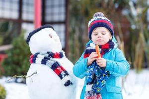 Funny kid boy faisant un bonhomme de neige en hiver à l'extérieur photo