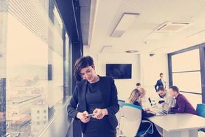 femme élégante utilisant un téléphone portable par fenêtre dans un immeuble de bureaux photo