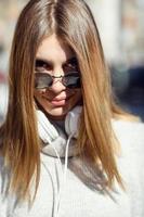 une fille moderne avec des lunettes de soleil marchant dans la rue écoute de la musique dans des écouteurs. photo