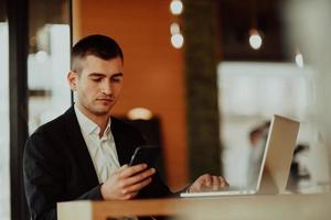 homme d'affaires heureux assis à la cafétéria avec ordinateur portable et smartphone.