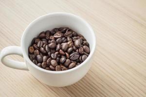 grains de café torréfiés frais dans une tasse blanche sur une table en bois