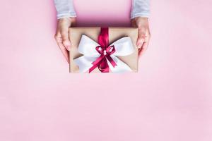 concept de noël de donner un cadeau. les mains des femmes dans un pull tenant une boîte-cadeau avec un arc. espace de copie de fond rose. photo