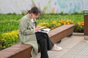 une fille est assise sur un banc dans la rue avec des documents dans les mains et utilise son téléphone photo