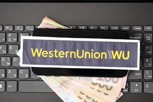 ternopil, ukraine - 6 septembre 2022 le logotype du papier western union se trouve sur un ordinateur portable noir avec des hryvnias ukrainiens. western union company est une multinationale américaine de services financiers photo