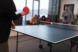deux jeunes hommes d'affaires en démarrage jouant au tennis de table dans un espace de bureau créatif moderne, un groupe de personnes se réunit et réfléchit en arrière-plan photo