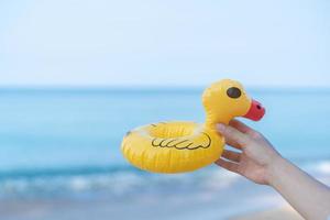 main tenant un canard jaune sur la plage avec une mer en arrière-plan. photo