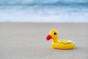 canard en caoutchouc jaune au bord de la mer le matin, plage de sable. photo