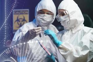 processus de test de coronavirus couple scientifique portant un masque médical avec des lunettes de sécurité en combinaison de matières dangereuses, tenant un tube d'échantillons de test sanguin à la main rapport avec des informations sur le test sanguin photo