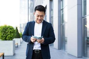 un homme asiatique compte de l'argent près du bureau, un homme d'affaires heureux a beaucoup d'argent photo