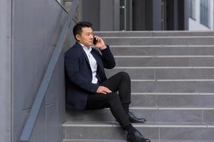 un courtier d'affaires asiatique rapporte de mauvaises nouvelles en parlant au téléphone, assis près du bureau photo