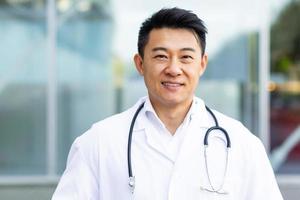 portrait d'un médecin asiatique gai souriant sur le fond d'une clinique moderne à l'extérieur photo