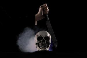 crâne humain halloween sur une vieille table en bois sur fond noir. forme d'os du crâne pour la tête de mort sur le festival d'halloween qui montre un couteau meurtrier tuant une phrase morte, espace de copie