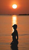 vue sur l'océan au coucher du soleil. soleil au-dessus de la mer sur ciel orange. femme debout sur la plage. photo