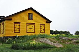 maison en bois jaune aux volets fermés parmi l'herbe verte, les fleurs jaunes et les grosses pierres photo