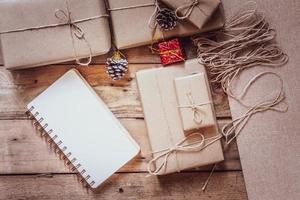 boîte-cadeau de noël utiliser du papier recyclé brun et un cahier et des pommes de pin sur une table en bois. photo