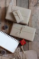 boîte-cadeau de noël utiliser du papier recyclé brun et un cahier et des pommes de pin sur une table en bois. photo