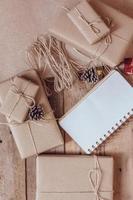 boîte-cadeau de noël utiliser du papier recyclé brun et un cahier et des pommes de pin sur une table en bois.