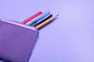 étui à crayons violet à la mode avec feutres multicolores, crayons et stylos sur fond lilas. photo