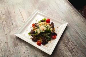 Salade César avec viande, feuilles et tomates sur plaque blanche