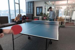 deux jeunes hommes d'affaires en démarrage jouant au tennis de table dans un espace de bureau créatif moderne, un groupe de personnes se réunit et réfléchit en arrière-plan photo