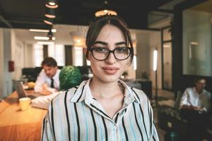 portrait d'une femme d'affaires en vêtements décontractés avec des lunettes à l'intérieur d'un bureau à aire ouverte de démarrage moderne. mise au point sélective photo