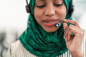 femme musulmane afro avec écharpe hijab verte représentante de la clientèle femme d'affaires avec casque téléphonique aidant et soutenant en ligne avec le client dans un centre d'appels moderne photo