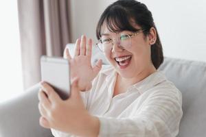 jeune femme asiatique utilisant un smartphone pour une visioconférence en ligne avec des amis agitant la main faisant un geste de bonjour photo