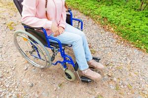 jambes pieds handicap femme en fauteuil roulant roue sur route dans le parc de l'hôpital en attente de services aux patients. fille paralysée méconnaissable dans une chaise invalide pour personnes handicapées à l'extérieur. notion de réhabilitation. photo