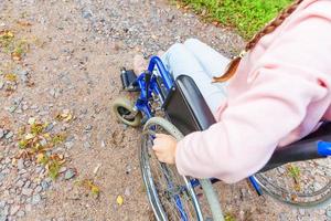 femme handicapée à la main dans la roue de fauteuil roulant sur la route dans le parc de l'hôpital en attente de services aux patients. fille paralysée méconnaissable dans une chaise invalide pour personnes handicapées à l'extérieur. notion de réhabilitation. photo