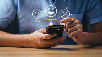 concept de satisfaction client et consommateur. les hommes d'affaires ou les clients expriment leur satisfaction par le biais d'une application sur l'écran d'un smartphone pour choisir 5 étoiles et emoji smiley photo