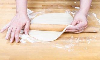 les mains étalent la pâte avec un rouleau à pâtisserie photo