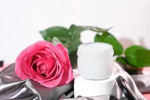 beurre corporel pour la peau hydratante et nourrissante. beurre parfumé à l'huile de rose dans un récipient en verre sur un piédestal à côté d'une rose rose fraîche. soins du corps de beauté. photo