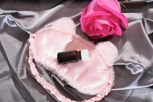 huile essentielle de pétale de rose dans une bouteille en verre ambré. masque de sommeil et fleur de rose sur des draps en satin de soie. bon sommeil, concept d'aromathérapie, remède naturel pour le traitement de la dépression, stress d'insomnie photo