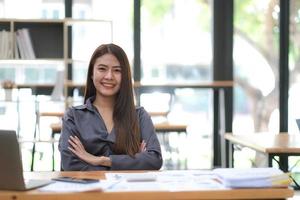 confiante jeune femme d'affaires asiatique assise avec les bras croisés souriant regardant la caméra au bureau. photo