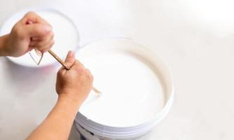 la main féminine utilise le bâton de bois pour mélanger la peinture dans le bac et tremper le rouleau. photo