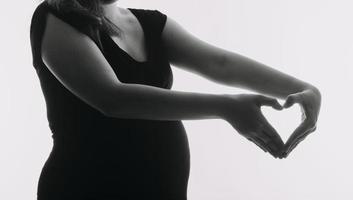 jeune femme enceinte adulte en vêtements blancs touchant un gros ventre nu avec les mains. montrant la forme. notion de grossesse. temps d'attente. fermer. isolé sur fond de mur gris clair. photo