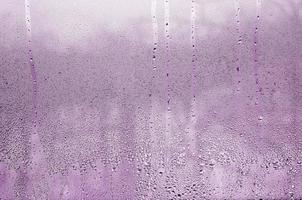 texture d'une goutte de pluie sur un fond transparent en verre humide. tonique en couleur rose photo