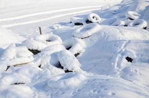 les pneus de voiture usagés et mis au rebut se trouvent sur le bord de la route, recouverts d'une épaisse couche de neige photo