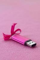 carte mémoire flash usb rose brillante avec un arc rose se trouve sur une couverture en tissu polaire rose clair doux et poilu. conception de cadeau féminin classique pour une carte mémoire photo