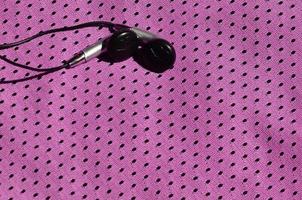les écouteurs noirs reposent sur les vêtements de sport violets en fibre de nylon polyester. le concept d'écouter de la musique pendant l'entraînement sportif avec la technologie moderne photo