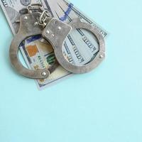 menottes de police en argent et billets de cent dollars se trouvent sur fond bleu clair photo