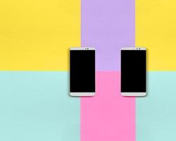 deux smartphones modernes avec écrans noirs sur fond de texture de papier de couleurs pastel bleu, jaune, violet et rose de mode dans un concept minimal photo
