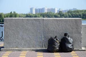 Deux sacs à ordures noirs sur le sol carrelé de la rue à la clôture en béton de la ville photo