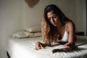 belle jeune femme se reposant sur son lit en lisant un livre. photo